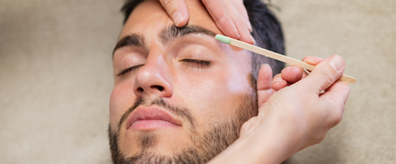 close up beautician waxing eyebrows of male client